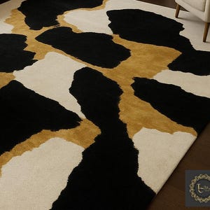 May include: A rectangular area rug with a bold, abstract design. The rug features large, irregular shapes in black, cream, and gold. The pattern creates a striking contrast, suitable for a modern living space. The rug is made of a soft material.