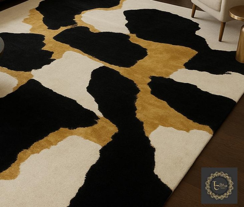 May include: A rectangular area rug with a bold, abstract design. The rug features large, irregular shapes in black, cream, and gold. The pattern creates a striking contrast, suitable for a modern living space. The rug is made of a soft material.