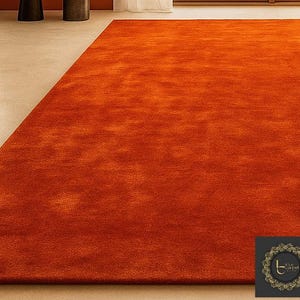 Op de afbeelding: Een groot, rechthoekig oranje tapijt met een zacht, getextureerd oppervlak. Het tapijt is effen van kleur en lijkt gemaakt van een zacht materiaal. Het tapijt ligt op een lichtgekleurde vloer, wat een warme en uitnodigende sfeer cre&euml;ert.