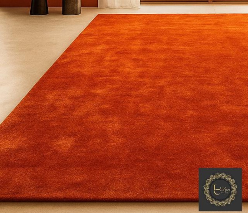 Op de afbeelding: Een groot, rechthoekig oranje tapijt met een zacht, getextureerd oppervlak. Het tapijt is effen van kleur en lijkt gemaakt van een zacht materiaal. Het tapijt ligt op een lichtgekleurde vloer, wat een warme en uitnodigende sfeer cre&euml;ert.