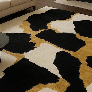 May include: A large area rug with a bold, abstract design. The rug features large black and gold shapes against a cream-colored background. A dark round coffee table and a cream-colored sofa are in the background.