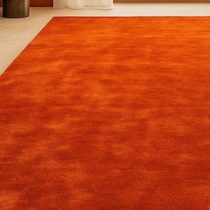 Op de afbeelding: Een groot, rechthoekig oranje tapijt met een getextureerd oppervlak. Het tapijt vult het grootste deel van het frame, met een klein deel van een lichtgekleurde vloer zichtbaar in de linkerbovenhoek. De kleur van het tapijt is een levendig, warm oranje.