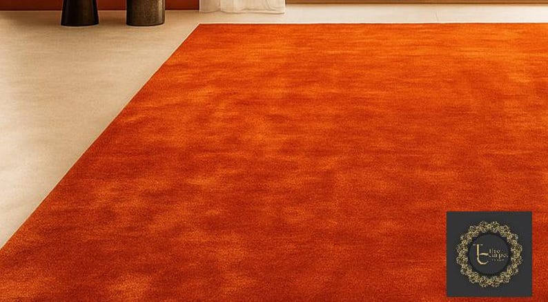 Op de afbeelding: Een groot, rechthoekig oranje tapijt met een getextureerd oppervlak. Het tapijt vult het grootste deel van het frame, met een klein deel van een lichtgekleurde vloer zichtbaar in de linkerbovenhoek. De kleur van het tapijt is een levendig, warm oranje.