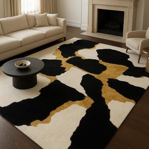 May include: A large area rug with a modern design. The rug features a cream-colored background with large, irregular shapes in black and gold. The rug is placed in a living room setting with a sofa, chairs, and a fireplace.