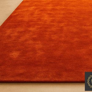 Op de afbeelding: Een close-up van een levendig oranje tapijt met een zacht, getextureerd oppervlak. De kleurovergang van het tapijt voegt diepte toe en de hoek onthult een contrasterend beige oppervlak. Het tapijt is een woondecoratie-artikel.