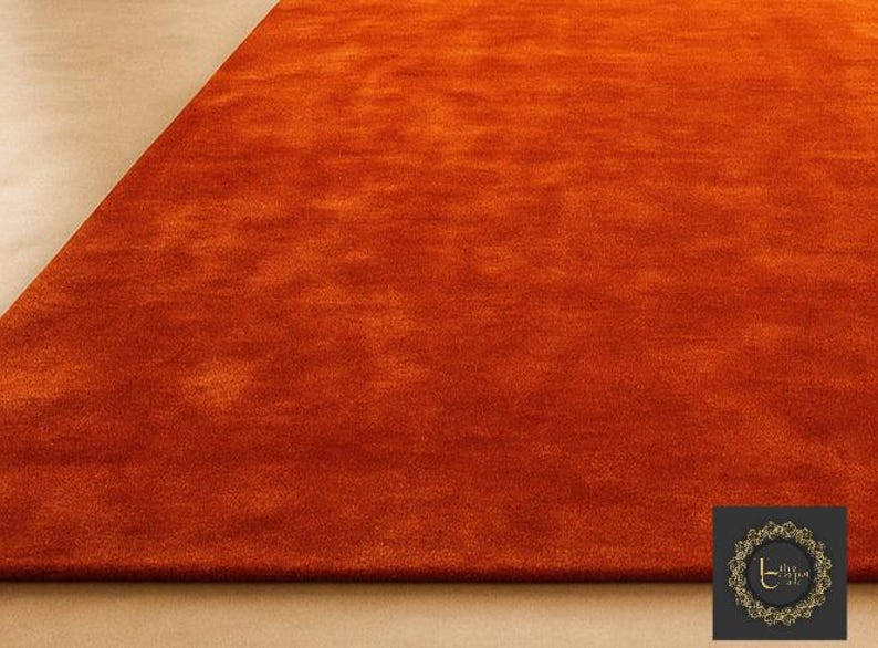 Op de afbeelding: Een close-up van een levendig oranje tapijt met een zacht, getextureerd oppervlak. De kleurovergang van het tapijt voegt diepte toe en de hoek onthult een contrasterend beige oppervlak. Het tapijt is een woondecoratie-artikel.