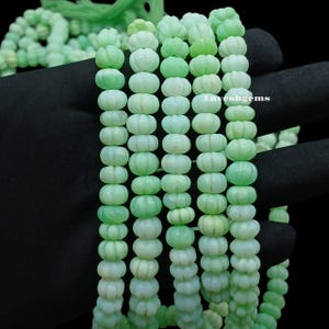 May include: Strands of light green gemstone beads with a pumpkin-like shape. The beads are strung together, creating a necklace or bracelet. The beads have a smooth, polished surface and a slight variation in color.