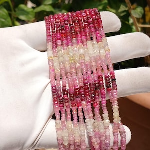 Puede incluir: Múltiples hilos de pequeñas piedras preciosas facetadas en tonos rosa, rojo y blanco. Las cuentas están ensartadas, creando un efecto en capas. Las piedras preciosas son sostenidas por una mano enguantada.