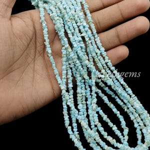 May include: A strand of small, irregular, light blue gemstone chips. The stones have a matte, opaque finish with subtle white and pale green variations throughout. The beads are strung together in a long, continuous line, creating a textured appearance.