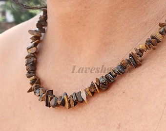 May include: A close-up of a necklace made of small, irregularly shaped tiger's eye stones. The stones are primarily brown with streaks of gold and black. The necklace is worn around the neck.