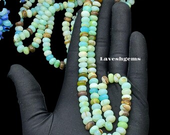 Könnte beinhalten: Stränge aus Edelsteinperlen in Grün-, Blau- und Brauntönen vor schwarzem Hintergrund. Die ovalen Perlen sind aufgereiht und bilden eine Halskette oder ein Armband. Der Text "Laveshgems" ist sichtbar.