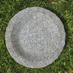 Può includere: Una pietra di passo rotonda e grigia con una superficie strutturata. La pietra è posizionata su un letto di erba verde. Un elemento naturale per esterni.