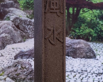 May include: A dark brown, rectangular stone pillar with the Japanese characters "風水" carved into it. The pillar is standing on a bed of green grass.