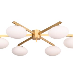 May include: A gold-toned ceiling light fixture with six white globe-shaped shades. The fixture has a modern, geometric design with a central hub and arms extending outwards.