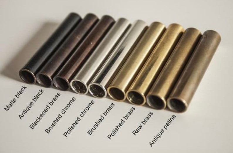 K&ouml;nnte beinhalten: Nahaufnahme von acht Metallrohren in verschiedenen Ausf&uuml;hrungen: mattschwarz, antikes Schwarz, geschw&auml;rztes Messing, geb&uuml;rstetes Chrom, poliertes Chrom, geb&uuml;rstetes Messing, poliertes Messing, rohes Messing und antike Patina.