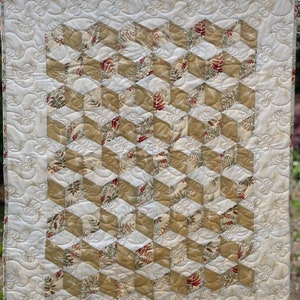 May include: A quilt with a geometric pattern of beige and white squares, with a floral print in the squares. The quilt is quilted with a swirling pattern.