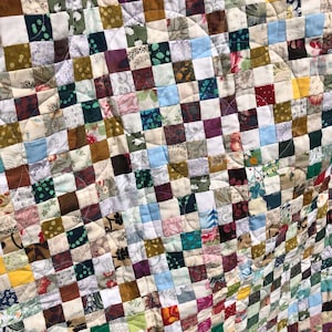 Puede incluir: Una colcha de patchwork que presenta una densa cuadrícula de pequeños cuadrados de tela multicolor con varios patrones, incluyendo estampados florales, geométricos y lisos. El tejido tiene un patrón de acolchado curvo continuo.