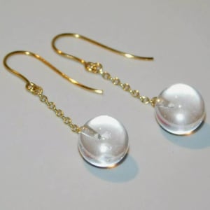 Puede incluir: Un par de pendientes de aro de oro con esferas de vidrio transparentes que cuelgan de delicadas cadenas.