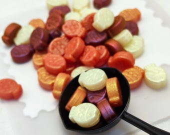Può includere: Una collezione di piccoli pezzi decorativi a forma di pesce in tonalità metalliche di bianco, arancione, rosso e viola. Alcuni pezzi sono sparsi, mentre altri sono contenuti in un piccolo misurino nero.