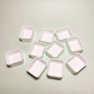 Pode incluir: Uma coleção de dez pequenas paletas de pintura brancas em forma quadrada. Cada paleta tem uma borda ligeiramente arredondada e um interior liso e vazio. As paletas estão espalhadas sobre uma superfície verde claro.