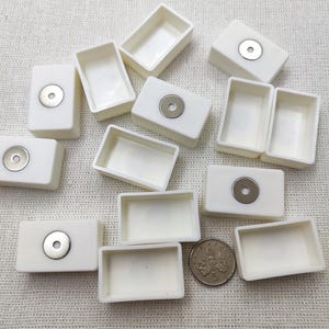 Pode incluir: Uma coleção de pequenas pastilhas retangulares brancas para aquarela. Algumas pastilhas têm um disco de metal prateado preso. Uma moeda está incluída para comparação de tamanho. As pastilhas estão vazias e prontas para uso.