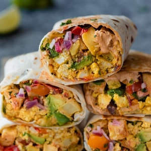 Może przedstawiać: Stos czterech śniadaniowych burrito wypełnionych jajecznicą, awokado, czerwoną cebulą i papryką. Burrito są zawinięte w białe tortille.