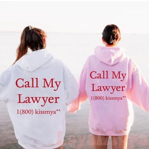 May include: Two people wearing matching hoodies with the text "Call My Lawyer 1(800) kissmya**" printed on the back. The hoodie on the left is white and the hoodie on the right is pink.