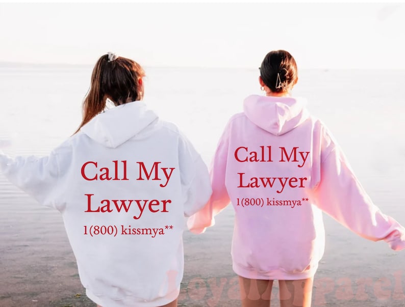 May include: Two people wearing matching hoodies with the text "Call My Lawyer 1(800) kissmya**" printed on the back. The hoodie on the left is white and the hoodie on the right is pink.