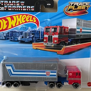 Puede incluir: Un camión de juguete Hot Wheels con el personaje de Transformers Optimus Prime. El camión es rojo, azul y plateado, con el logotipo de Transformers. El embalaje incluye los logotipos de Hot Wheels y Transformers, y el texto "Track Fleet".