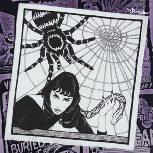 Peut inclure: Illustration en noir et blanc d'une femme, d'une araignée et d'un serpent. La femme tient le serpent. Un toile d'araignée est en arrière-plan, avec le texte "The Scream You".