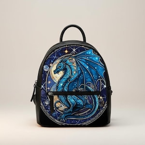 May include: Black backpack featuring a blue dragon design. The dragon has blue wings and is set against a background of a moon and stars. The backpack has a top handle and a zippered front pocket.
