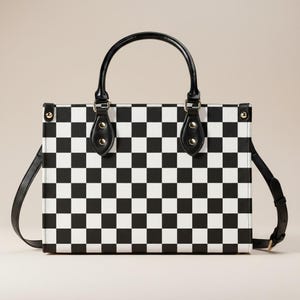 May include: A rectangular handbag with a black and white checkerboard pattern. The bag has a black handle and a detachable black shoulder strap. The handle is attached with black leather accents and gold-colored rivets.