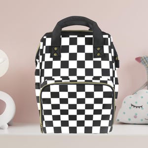 Puede incluir: Bolso de pañales a cuadros blanco y negro con cremalleras doradas y asas negras.