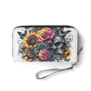 May include: White wallet with a black zip and wrist strap. The wallet features a colourful floral and skull design with sunflowers, roses, and butterflies. The design is in shades of yellow, pink, grey, and black.