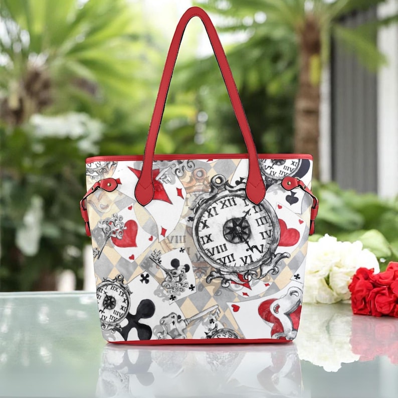 Puede incluir: Una bolsa de mano blanca con ribete rojo y un dise&ntilde;o de cartas de juego, relojes y otros elementos caprichosos. La bolsa tiene dos asas rojas.
