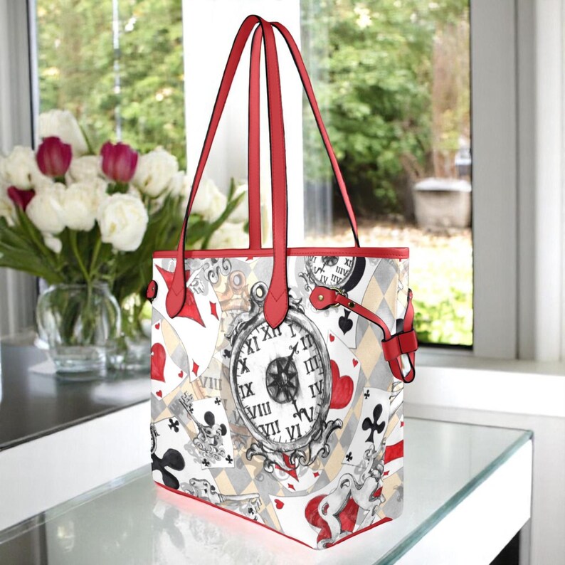 Puede incluir: Una bolsa de mano roja y blanca con un dise&ntilde;o caprichoso que presenta cartas de juego, un reloj y un patr&oacute;n a cuadros. La bolsa tiene asas rojas.