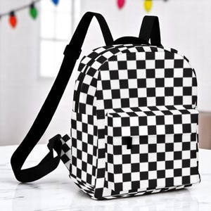 May include: A black and white checkered backpack with adjustable black straps and a front pocket. The backpack has a classic checkerboard pattern and a zippered main compartment. The bag is designed for carrying books and other school supplies.
