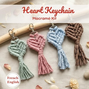 Può includere: Quattro portachiavi a forma di cuore in macramè, nei colori verde, rosa, blu e marrone, ciascuno con chiusura argentata e nappina. L'immagine include il testo "Heart Keychain Macramé Kit". Un kit fai-da-te.