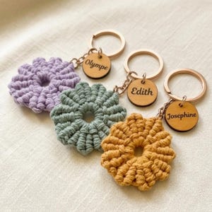 Peut inclure: Quatre porte-clés faits à la main en forme de fleurs au crochet, dans les tons de violet, de vert et d'or. Chaque porte-clés comporte une étiquette en bois gravée d'un nom. Les porte-clés ont des anneaux en métal doré.