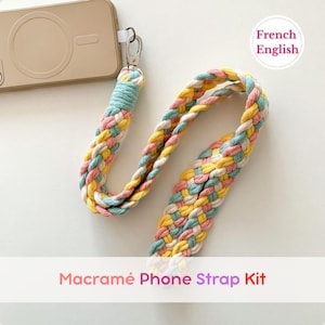 Peut inclure: Un kit de lanière de téléphone macramé aux couleurs pastel, jaune, rose, bleu et blanc. La lanière tressée est fixée à une coque de téléphone par un fermoir argenté. Le texte "Macramé Phone Strap Kit" est affiché.