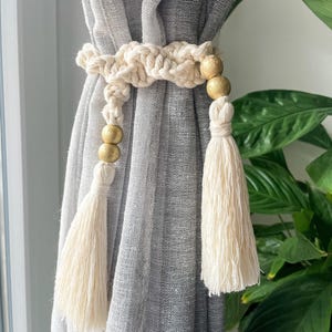 フリンジとゴールドの木製ビーズが付いたマクラメカーテンタイバック。エレガントなカーテンホールドバック。