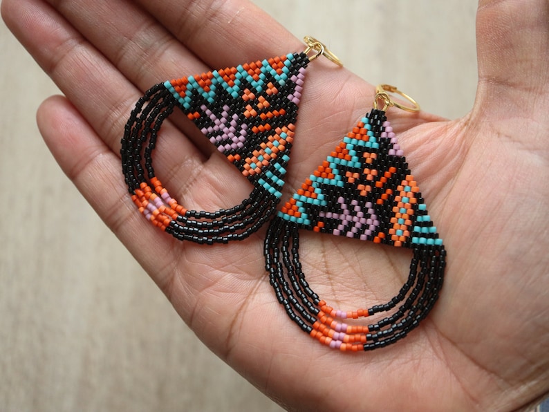 May include: A pair of beaded earrings with a geometric triangle design in black, orange, pink, and turquoise. The earrings have a fringe of black beads with orange and pink accents.