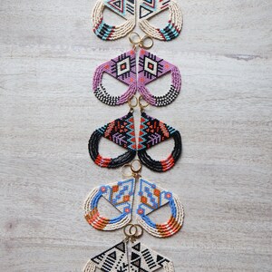 May include: Five pairs of beaded earrings with geometric patterns in various colors, including black, white, blue, orange, and pink. The earrings are all in the shape of a triangle with a fringe.