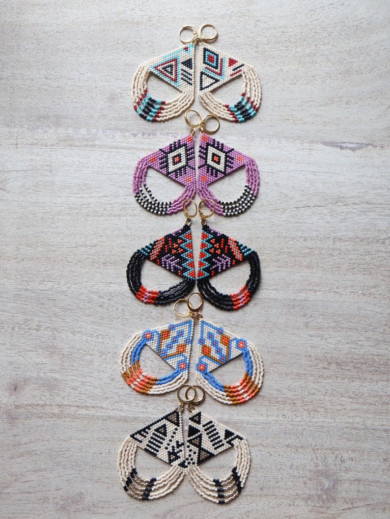 May include: Five pairs of beaded earrings with geometric patterns in various colors, including black, white, blue, orange, and pink. The earrings are all in the shape of a triangle with a fringe.