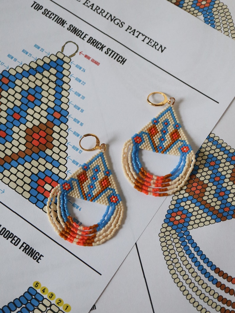 May include: A pair of beaded earrings with a geometric pattern in shades of blue, orange, and white. The earrings are made with small beads and have a fringe at the bottom. The earrings are shown on a white background with a diagram of the beading pattern.
