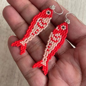 以下が含まれることがあります： 銀色のフックが付いた赤とピンクのビーズでできた魚のイヤリングのペアです。