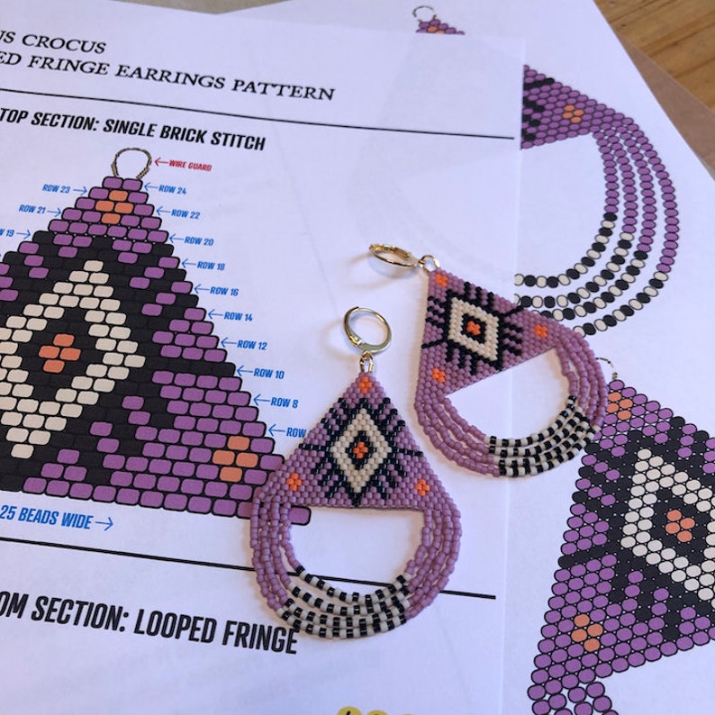 May include: A pair of purple and white beaded earrings with a geometric design. The earrings are made with a single brick stitch and have a looped fringe. The earrings are shown on a printed pattern for making the earrings.