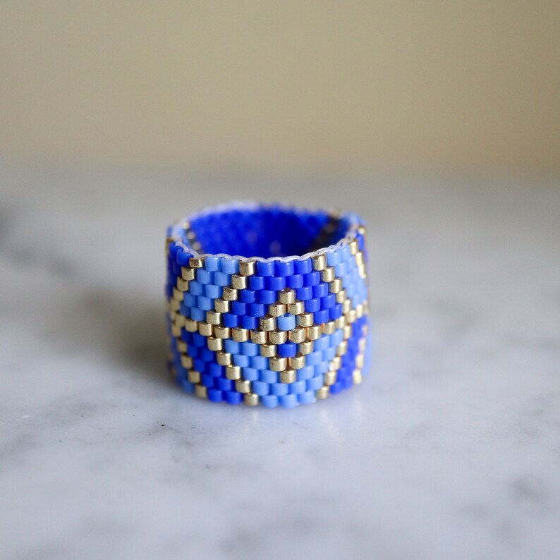 May include: A blue and gold beaded ring with a geometric pattern. The ring is made of small, colorful beads and is a unique piece of jewelry.