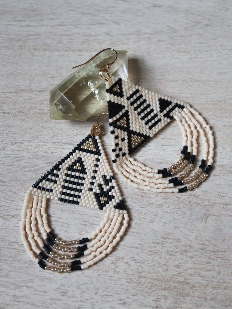 May include: A pair of black, white, and gold beaded earrings with a geometric pattern and fringe.
