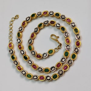 Può includere: Una collana d'oro con una catena e pietre di forma ovale. Le pietre sono incastonate in oro e sono di colore bianco, verde e rosa.